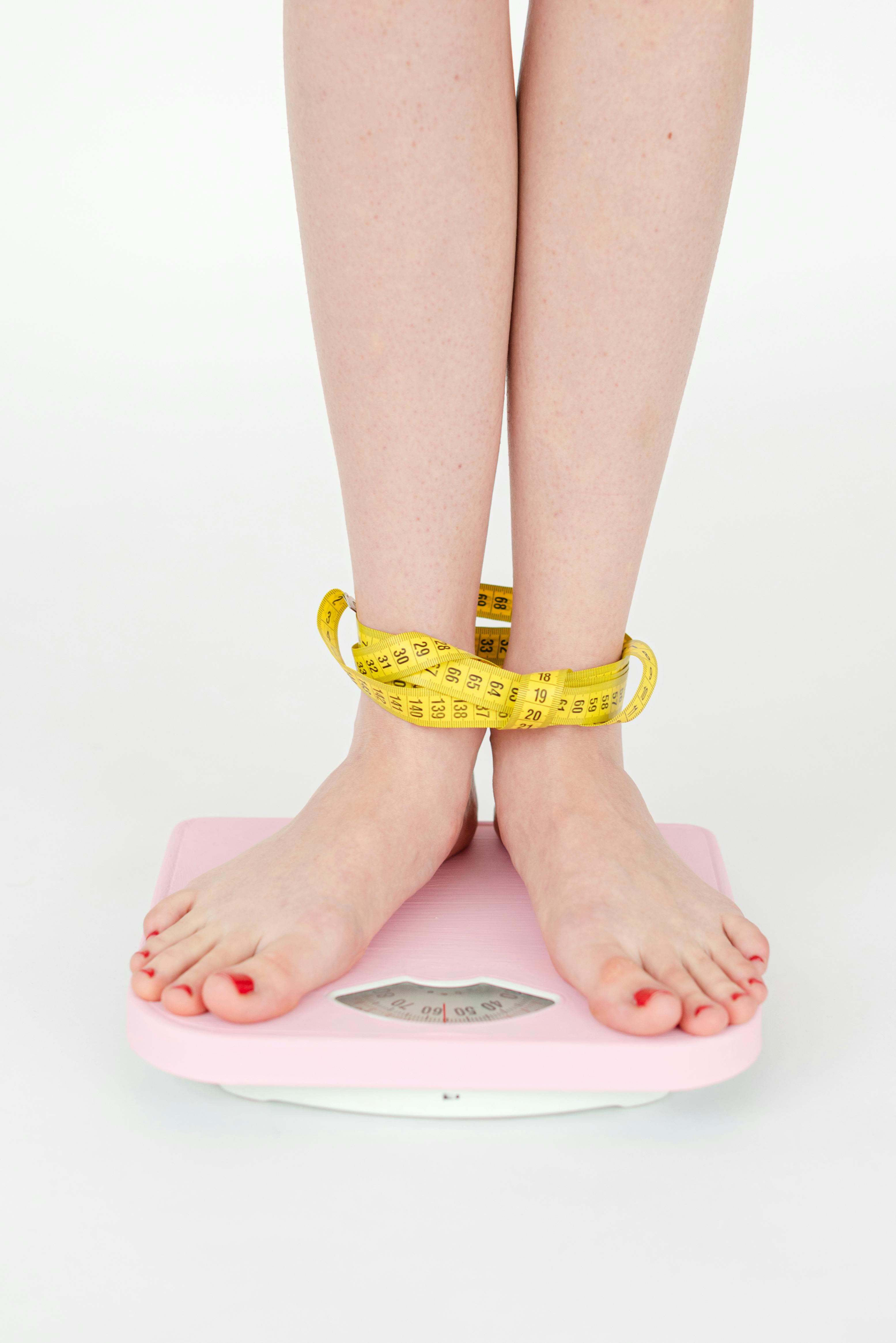 Close-up of a woman's feet on a pink scale wrapped in measuring tape, symbolizing weight management.